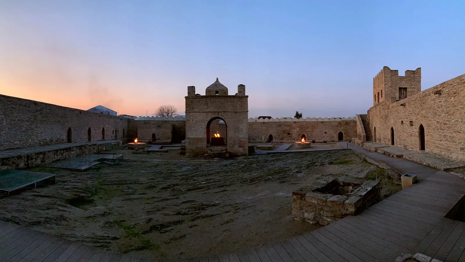 The courtyard of the Ateshgah fire temple at dusk, flames burning in the central pavilion.